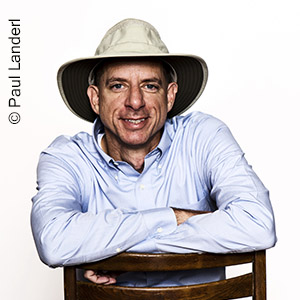 Mann mit weißem Hut und hellblauem Hemd blickt frontal in die Kamera John Strelecky